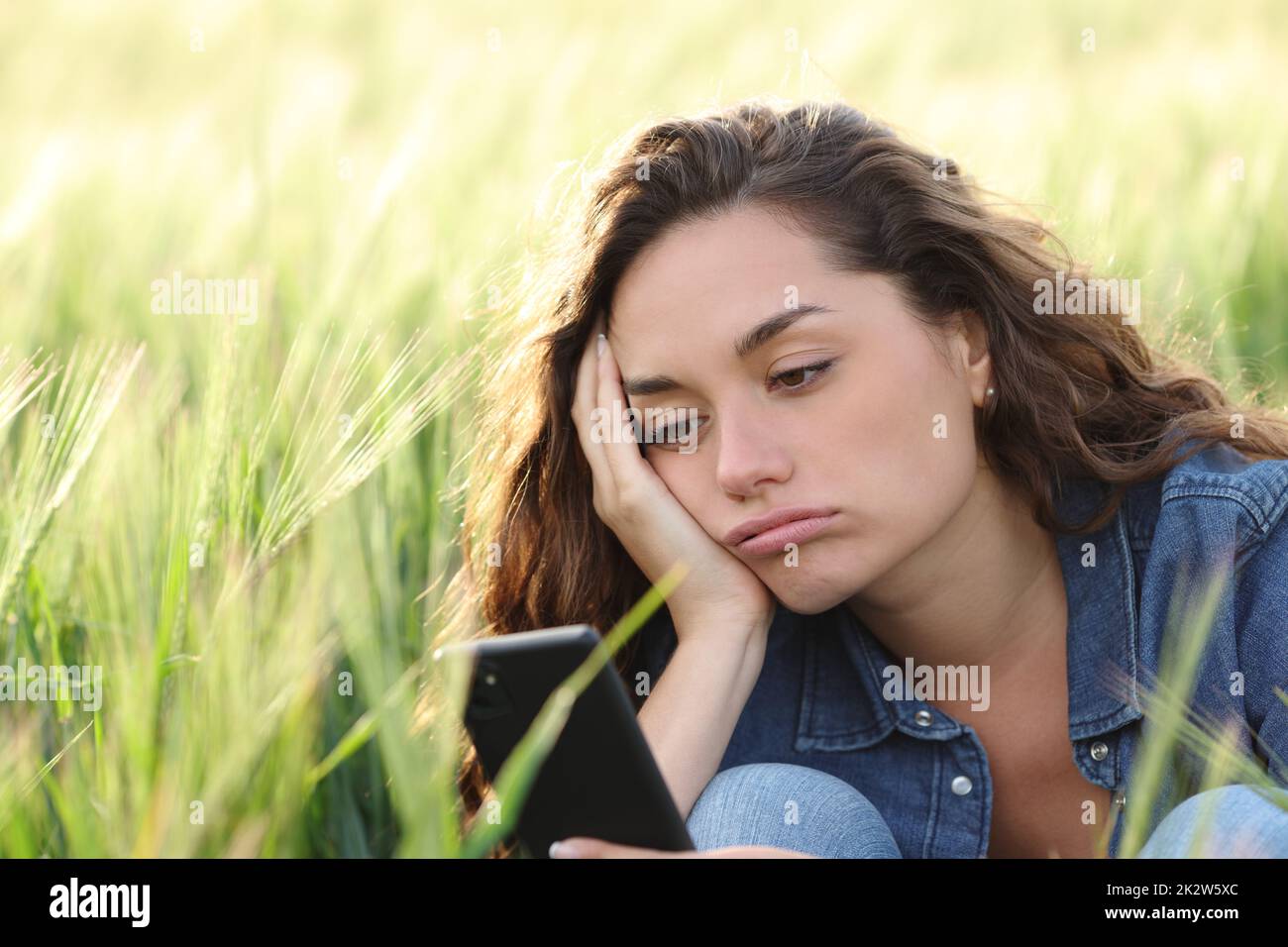 Annoiato donna che controlla il telefono in un campo di grano Foto Stock