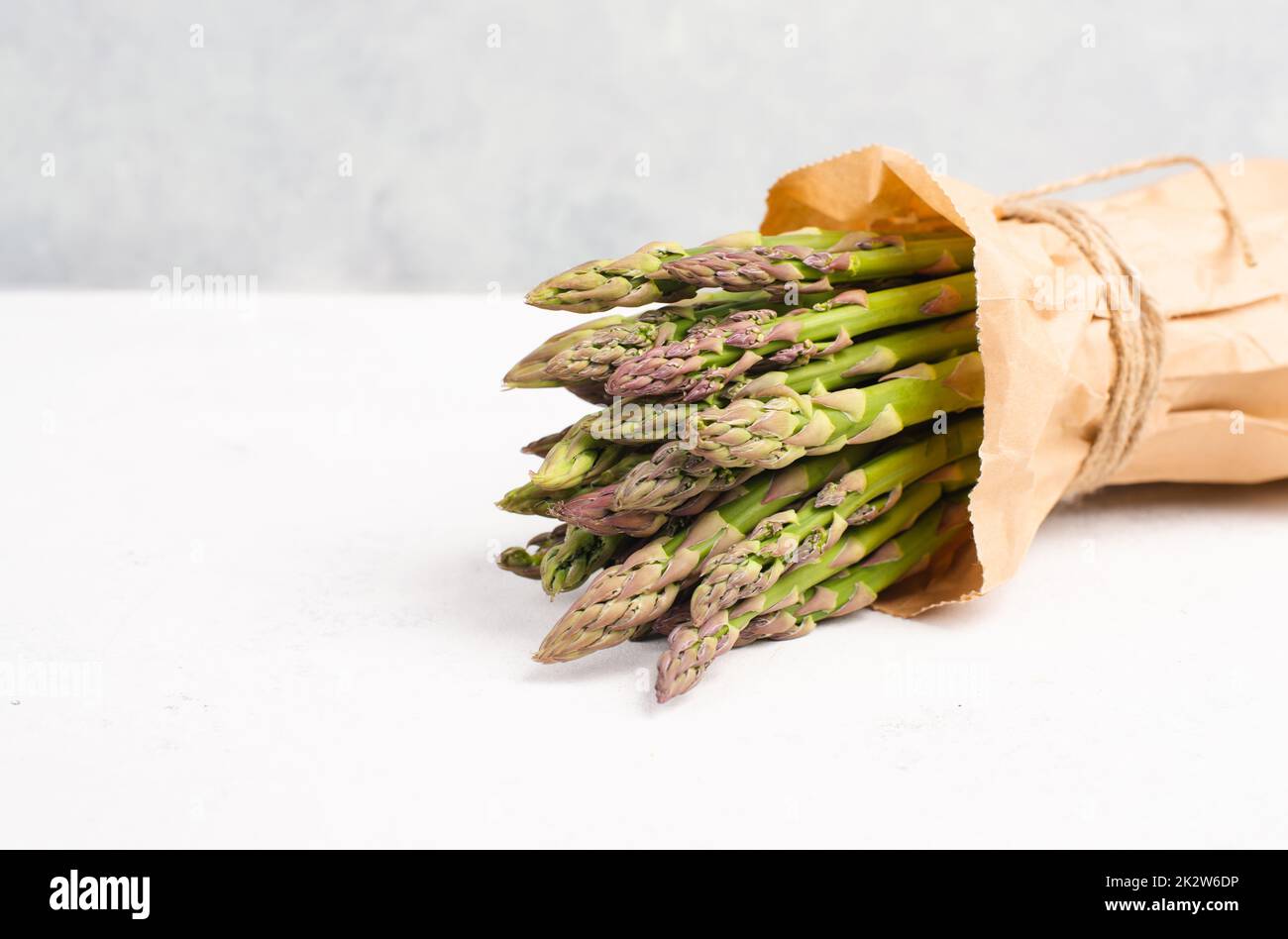 Pacco verde di asparagi freschi su un tavolo bianco testurizzato, verdure in primavera, cibo gourmet cucina, la cottura di un pasto vegano Foto Stock