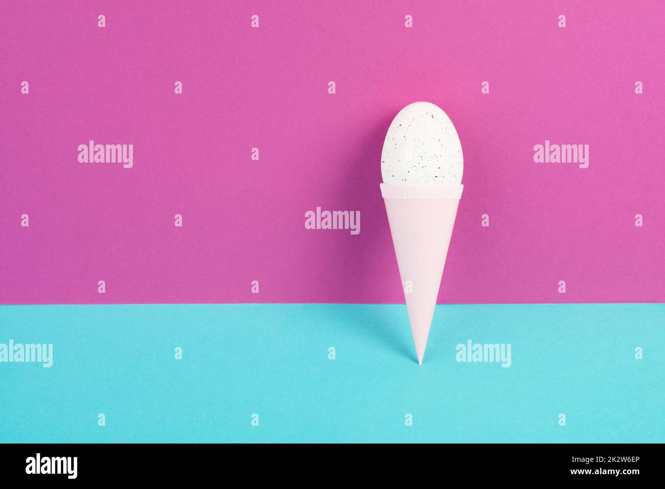 Cono gelato con uovo, sfondo rosa e blu, spazio copia, vacanze di pasqua, stagione estiva, minimalismo e concetto creativo, biglietto di auguri Foto Stock