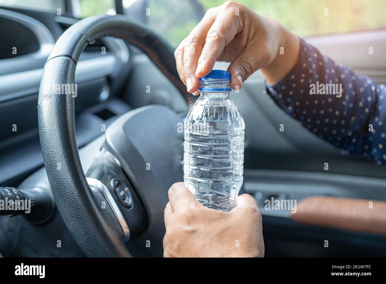 Donna asiatica conducente che tiene una bottiglia per bere acqua mentre guida una macchina. La bottiglia di plastica dell'acqua calda provoca un incendio. Foto Stock