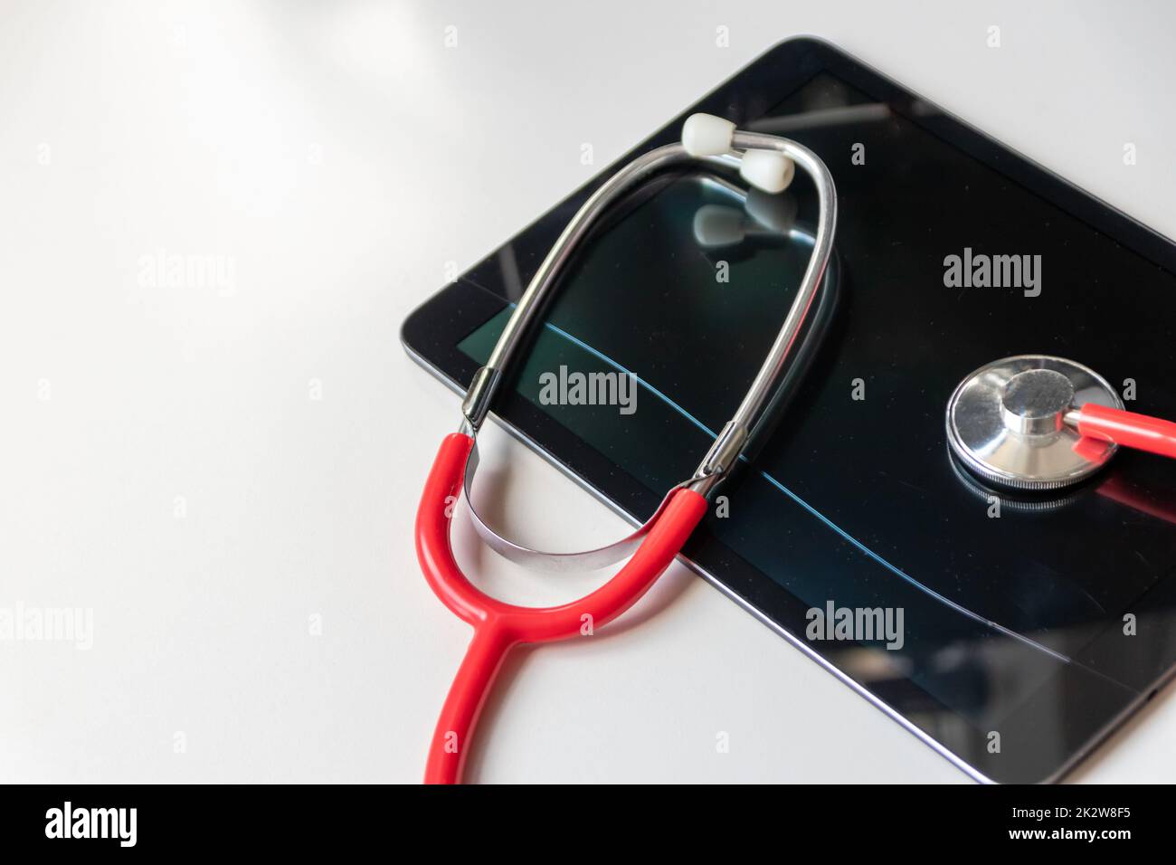 Lo stetoscopio rosso sul dispositivo tablet nero mostra le cartelle cliniche e le cartelle digitali dei pazienti sulla sicurezza dei dati sul cloud per i medici digitali e la diagnostica del recupero digitale con apparecchiature e tecnologie moderne Foto Stock