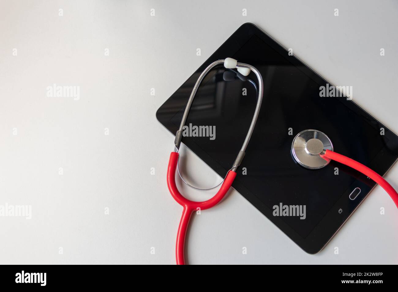 Lo stetoscopio rosso sul dispositivo tablet nero mostra le cartelle cliniche e le cartelle digitali dei pazienti sulla sicurezza dei dati sul cloud per i medici digitali e la diagnostica del recupero digitale con apparecchiature e tecnologie moderne Foto Stock