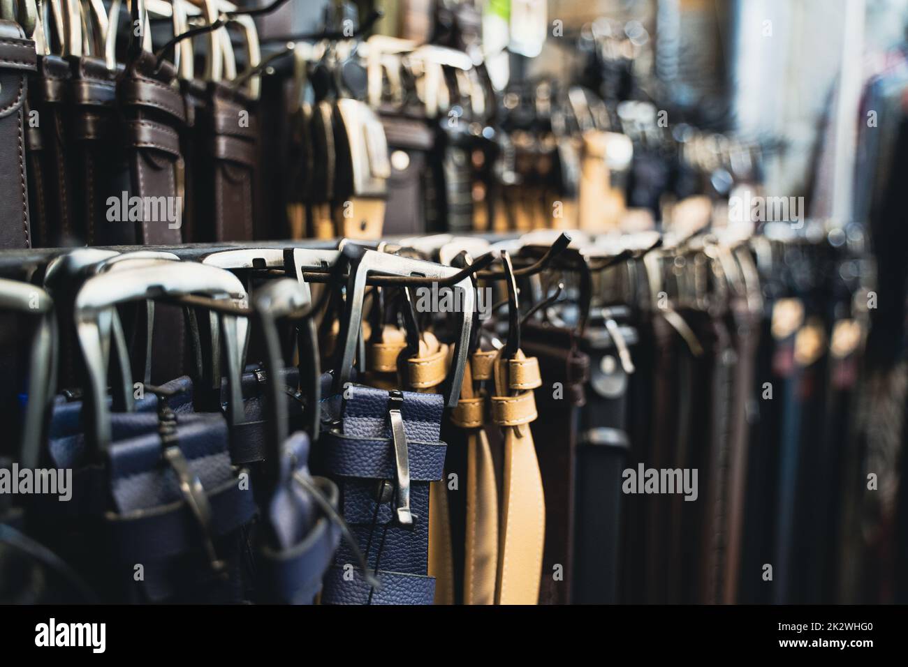 vista prospettica primo piano di diversi tipi di cinture colorate in pelle per jeans e tute pantaloni appesi alla fibbia in mostra negozio di abbigliamento Foto Stock