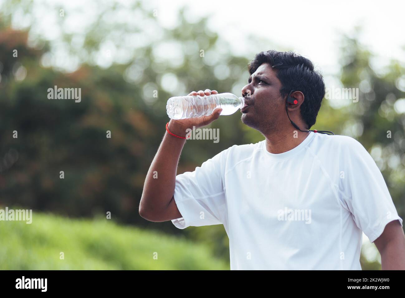 sport runner uomo nero indossa le cuffie dell'atleta che beve acqua da una bottiglia Foto Stock