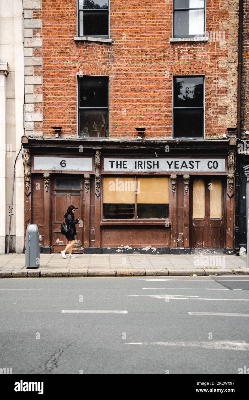Un colpo verticale di una donna in nero a piedi dalla vecchia Irish Yeast Company nelle strade di Dublino Foto Stock
