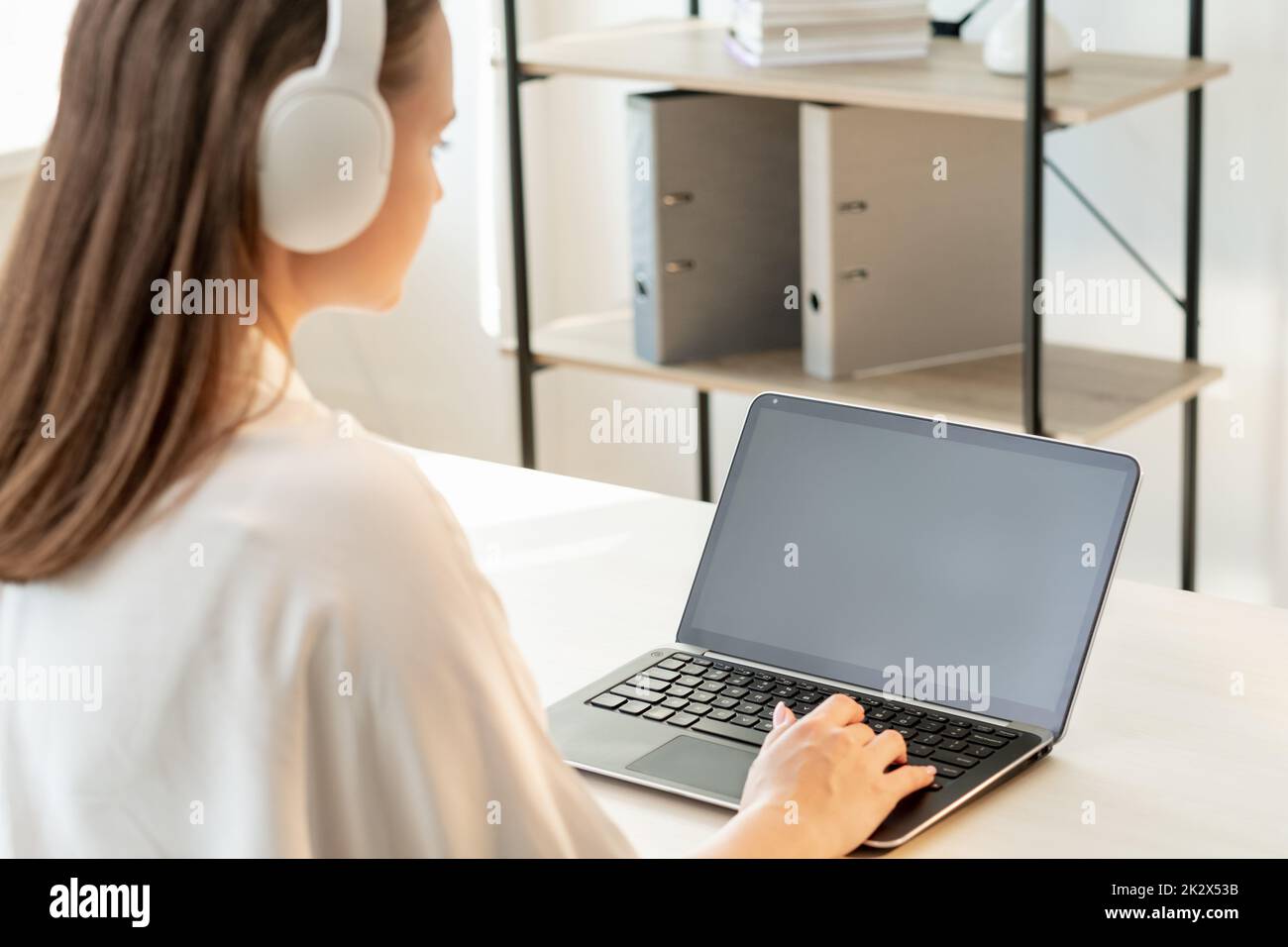 Istruzione remota. Apprendimento a distanza. Comunicazione online. Videoconferenza. Donna con cuffie wireless bianche che utilizzano notebook con schermo nero vuoto Foto Stock