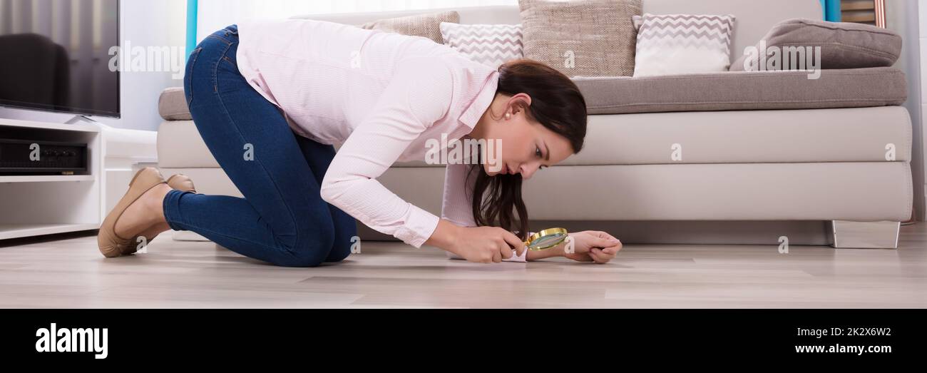 Donna che guarda al pavimento di legno attraverso la lente di ingrandimento Foto Stock