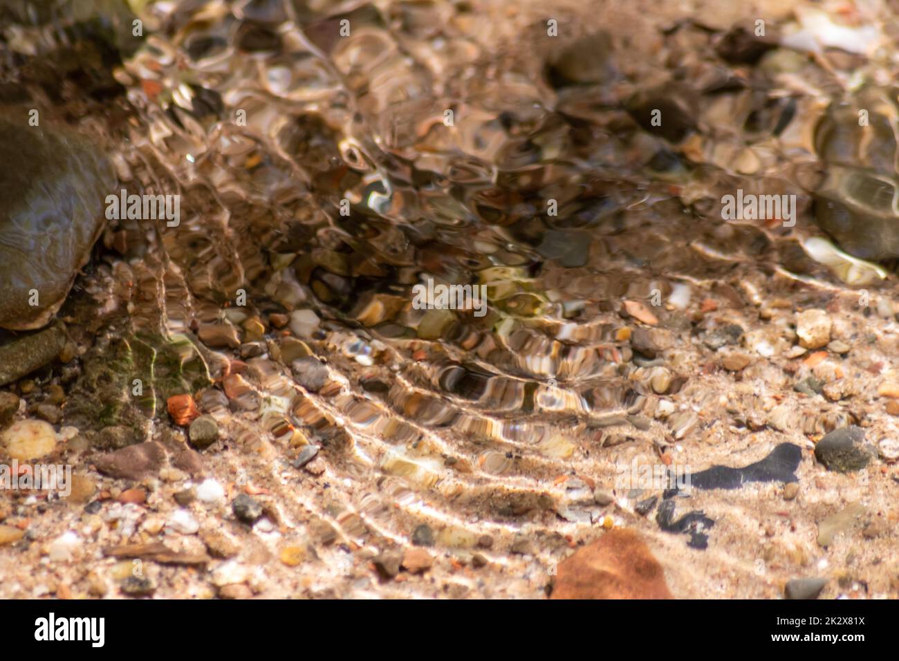 Pietre in acqua frizzante con riflessi soleggiati in acqua di un torrente di acqua cristallina come idilliaco sfondo naturale mostra zen meditazione, piccole onde e ondate setose in una sorgente di montagna sana Foto Stock