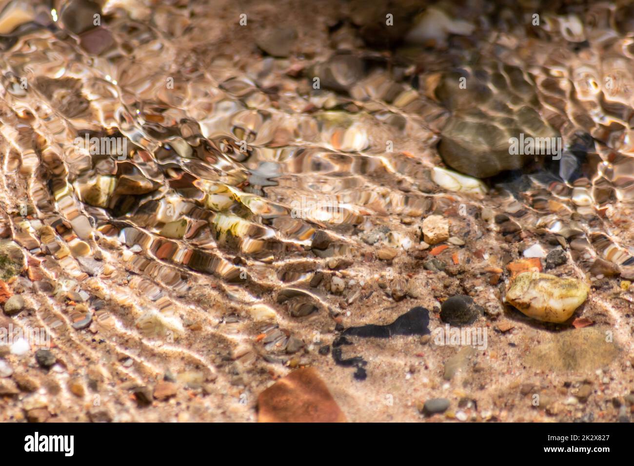 Pietre in acqua frizzante con riflessi soleggiati in acqua di un torrente di acqua cristallina come idilliaco sfondo naturale mostra zen meditazione, piccole onde e ondate setose in una sorgente di montagna sana Foto Stock
