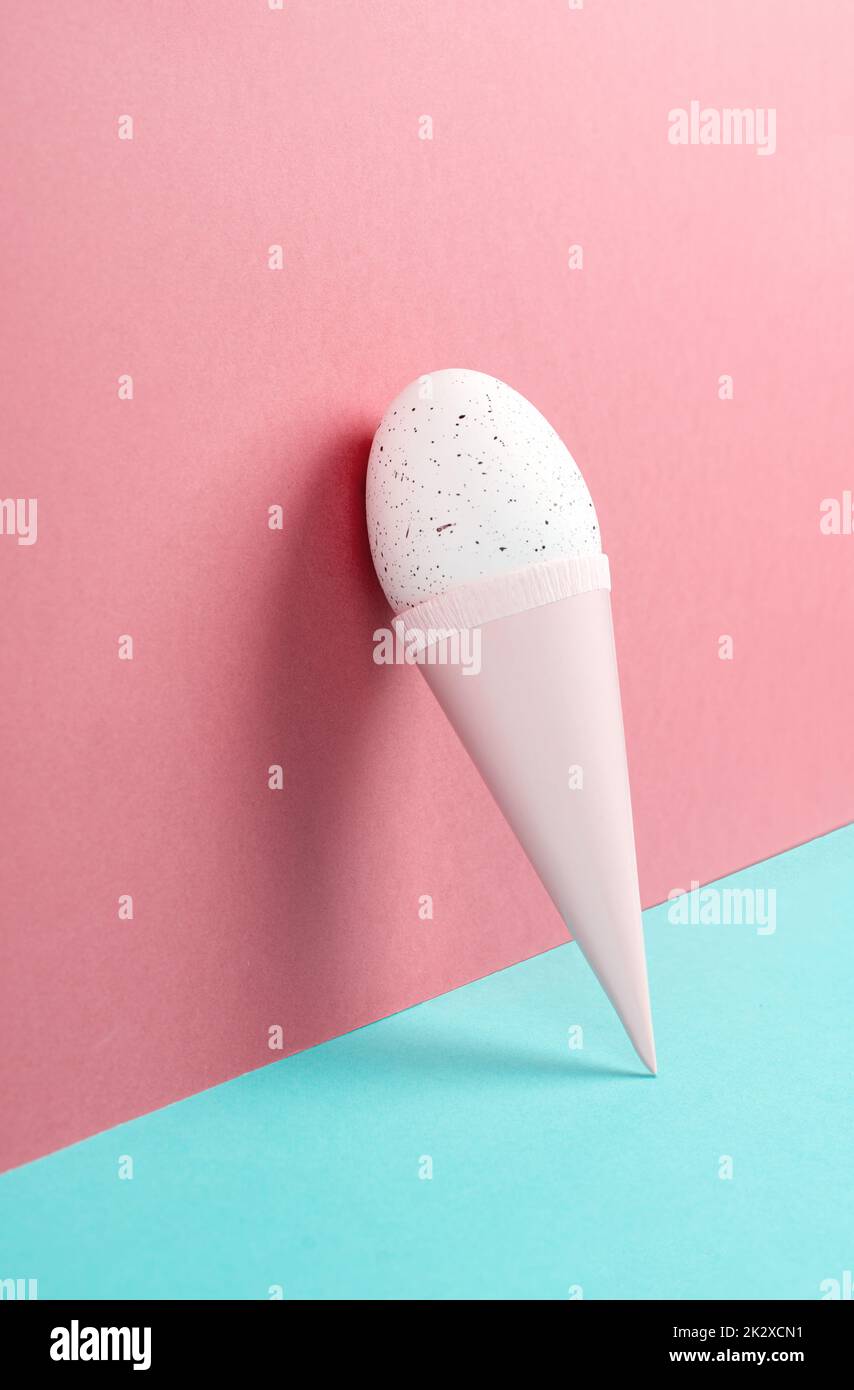 Cono gelato con uovo, sfondo rosa e blu, spazio copia, vacanze di pasqua, stagione estiva, minimalismo e concetto creativo, biglietto di auguri Foto Stock