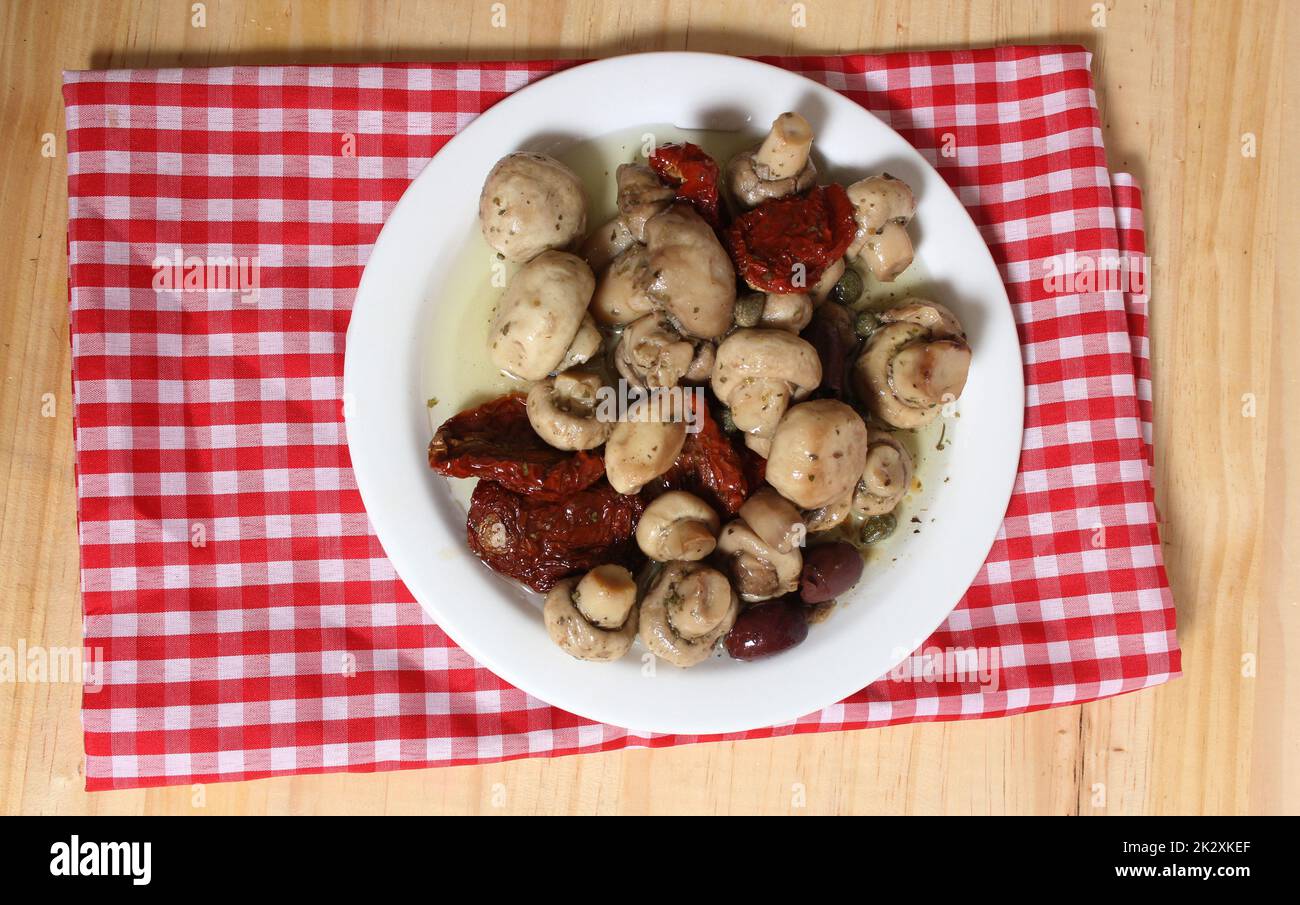 Funghi, pomodori secchi, olive e capperi in olio d'oliva su tavola rustica Foto Stock