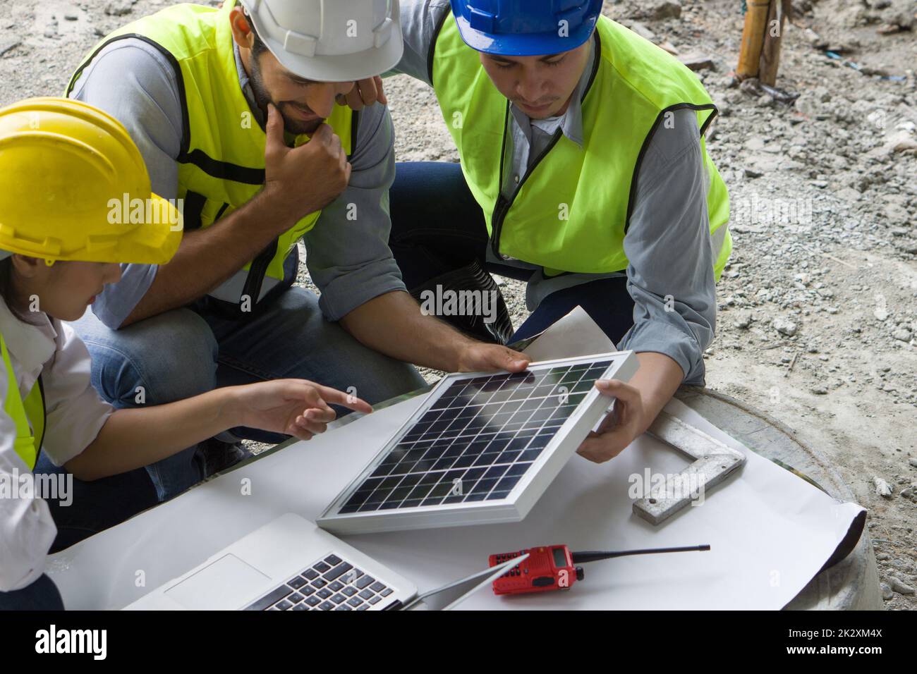 Progetto di costruzione immobiliare meeting su tavolo in betoniera. Le mani umane, il computer portatile, il pannello a celle solari, il walkie-talkie e la piazza dell'ingegnere sono su white paper. Foto Stock