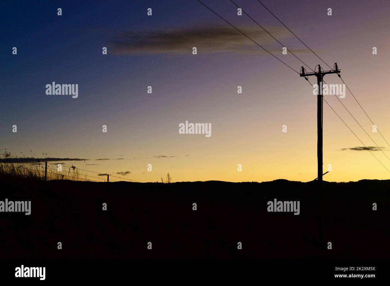 Poli di potenza da una strada di campagna al tramonto Foto Stock