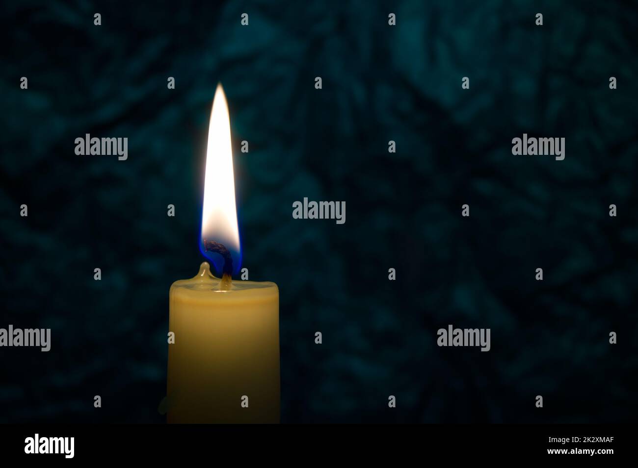 Singola candela di cera gialla che brucia da sola al buio Foto Stock