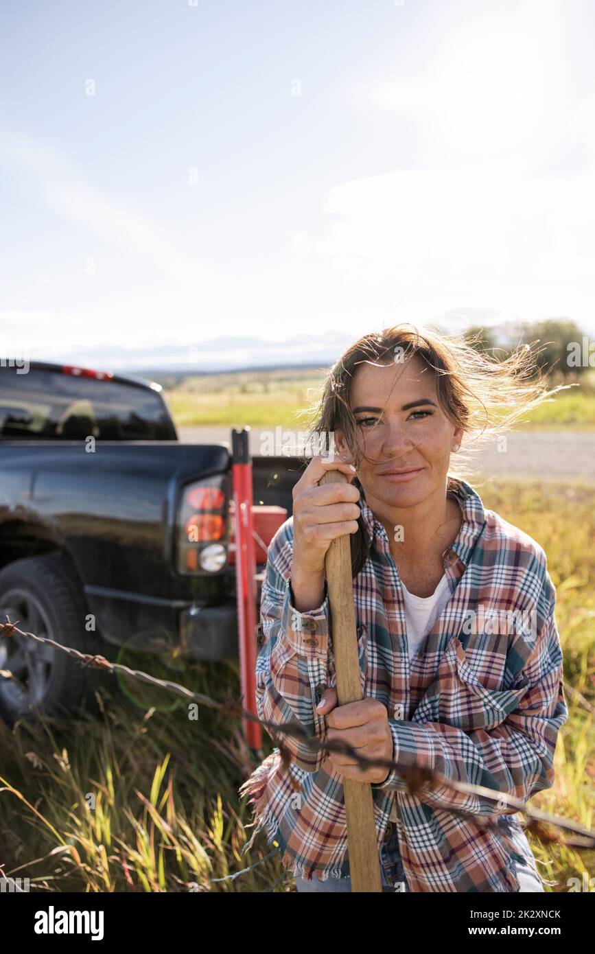 Ritratto fiducioso femmina rancher a spinato filo recinto su ranch soleggiato Foto Stock