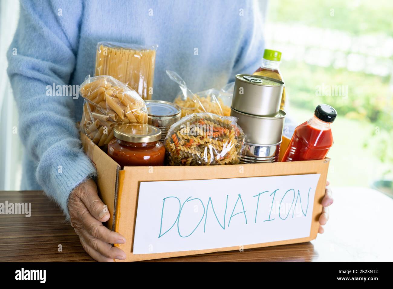 Volontari che mettono vari alimenti secchi in scatola di donazione per aiutare le persone. Foto Stock