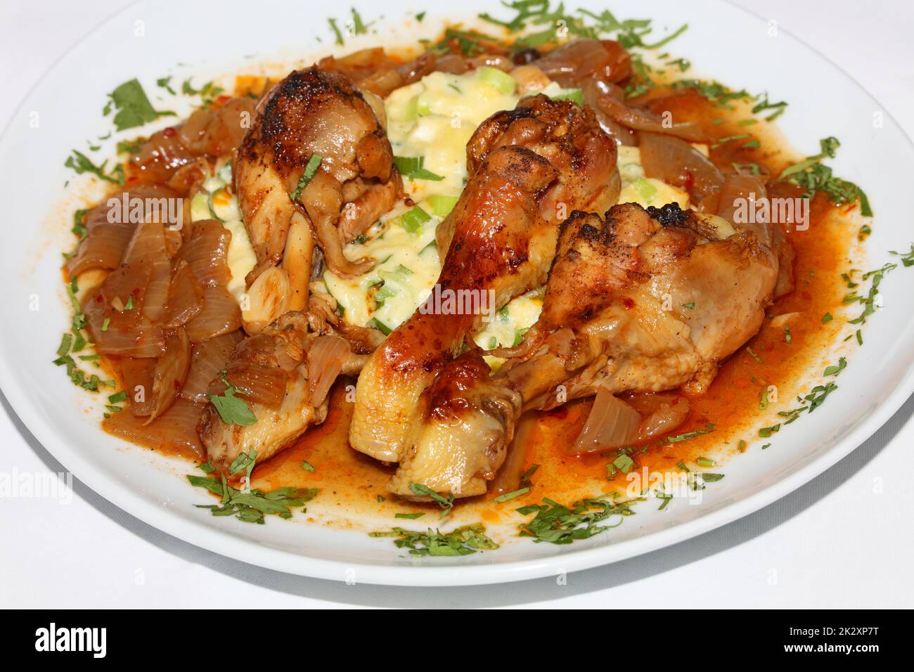 Cosce di pollo primo piano brasate con cipolle di macellaio servite con purè di patate alle erbe cucina greca moderne stampe di alta qualità Foto Stock