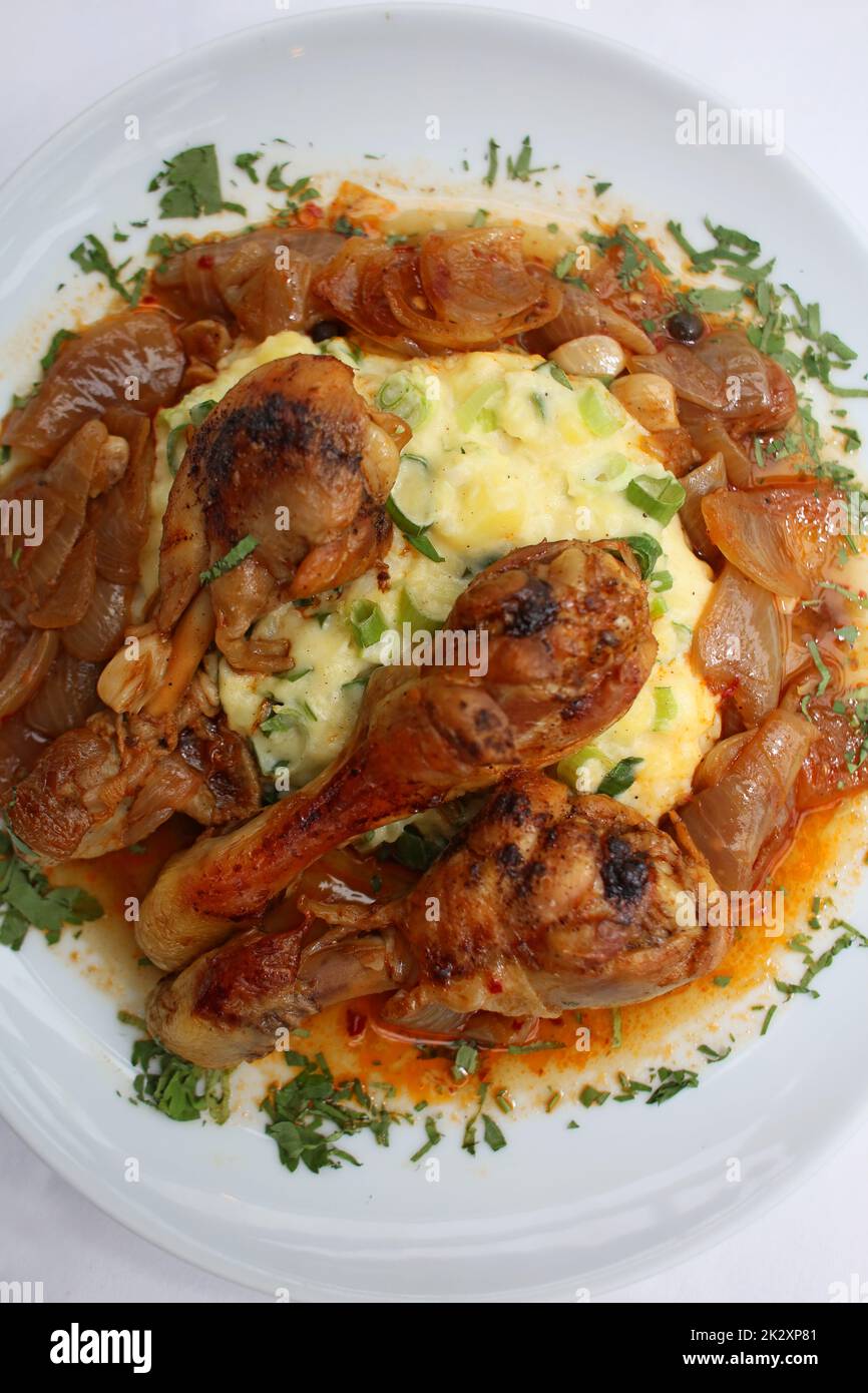 Cosce di pollo primo piano brasate con cipolle di macellaio servite con purè di patate alle erbe cucina greca moderne stampe di alta qualità Foto Stock