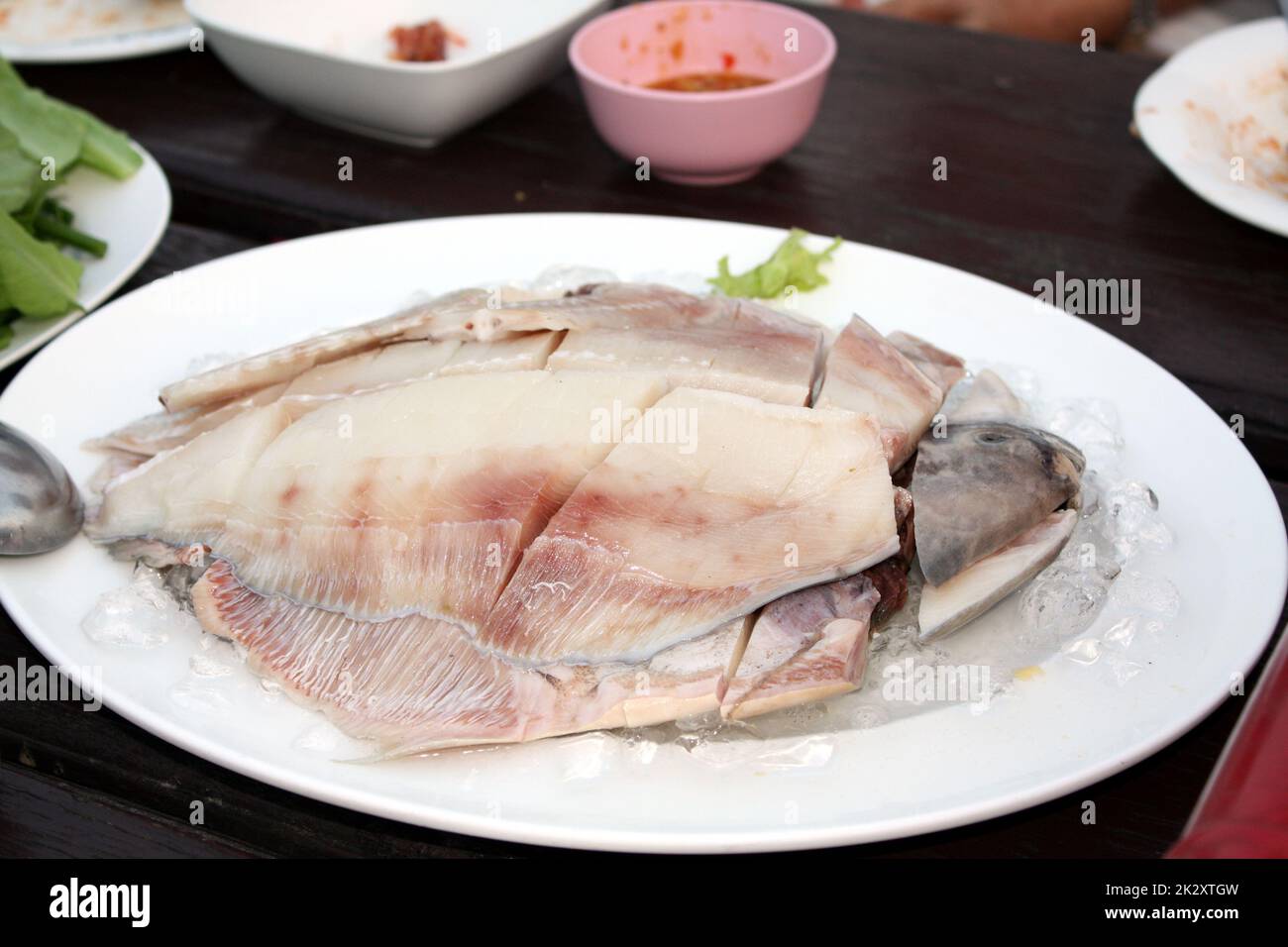 FRESH Gray pomfret, pesce cinese al pomfret d'argento tagliato a pezzi sistemato in un piatto bianco sormontato di ghiaccio. Sul tavolo di legno del ristorante, preparare per la pentola di shabu. Messa a fuoco selettiva. Foto Stock