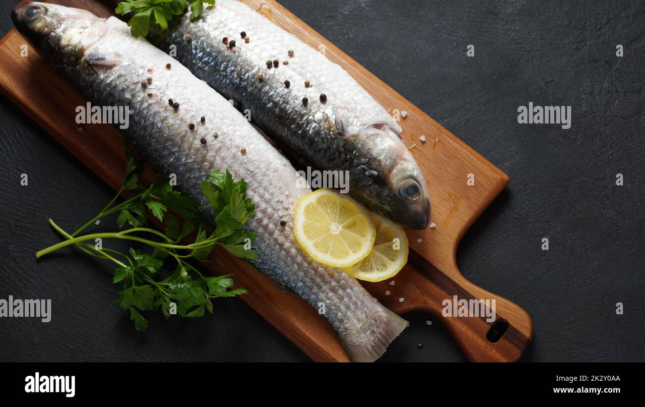 Pesce fresco triglie con lime, erbe e spezie su sfondo scuro. Foto Stock