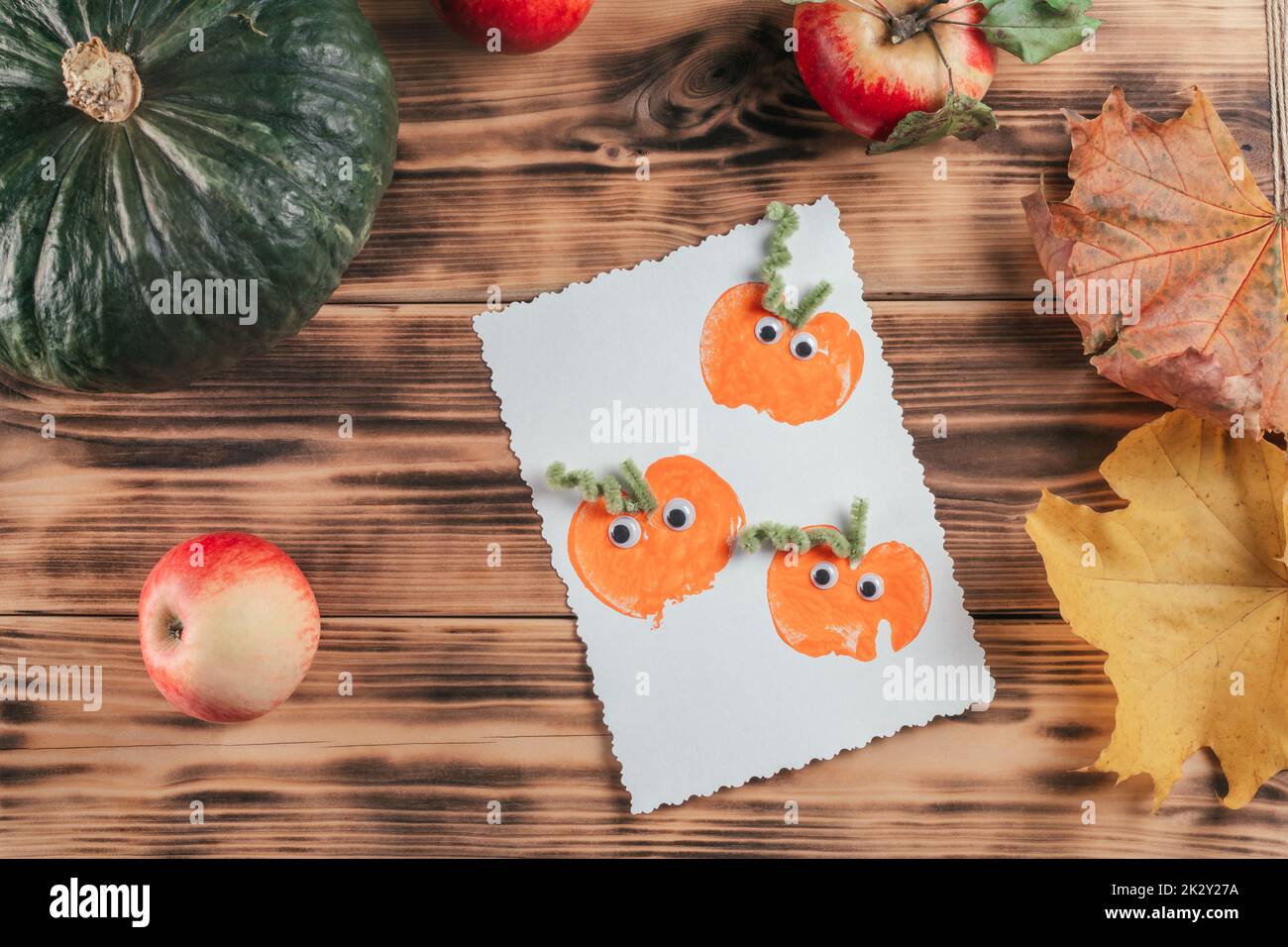 Carta di Halloween pronta all'uso con stampe di zucca di mela si trova accanto alle mele e foglie autunnali su superficie di legno. Vista dall'alto Foto Stock