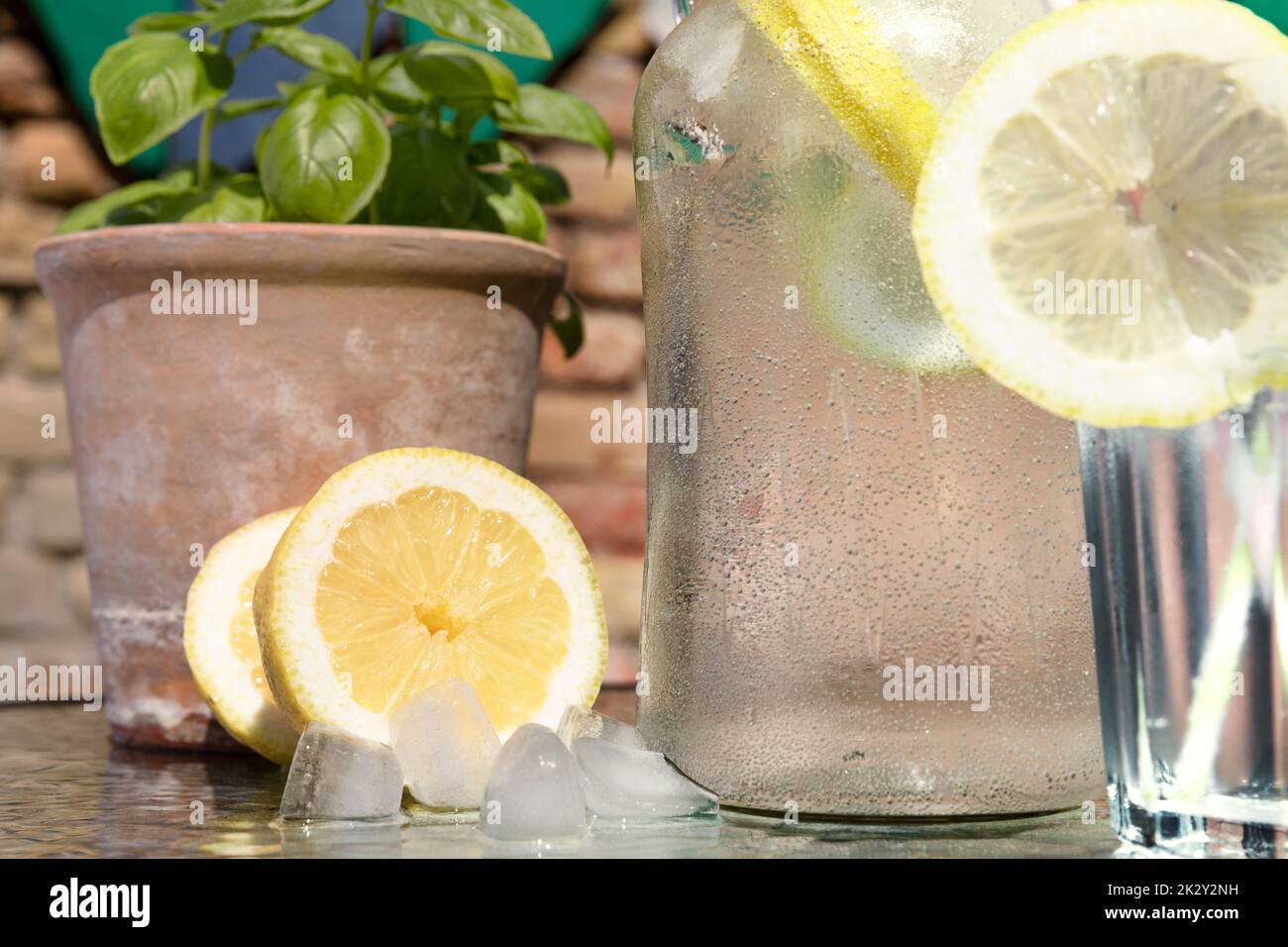 Acqua fresca e fredda in una calda giornata estiva con cubetti di ghiaccio e limone. Concetto di disidratazione del calore. Messo di fronte a vecchio muro di mattone. Foto Stock