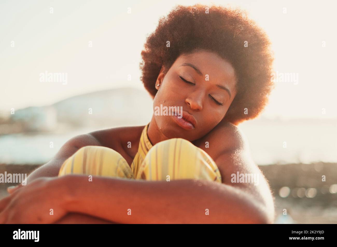Ritratto anteriore di bella giovane ragazza nera rilassante con gli occhi chiusi all'aperto con la luce del sole sullo sfondo. Concetto di meditazione gente serena. Lovin Foto Stock