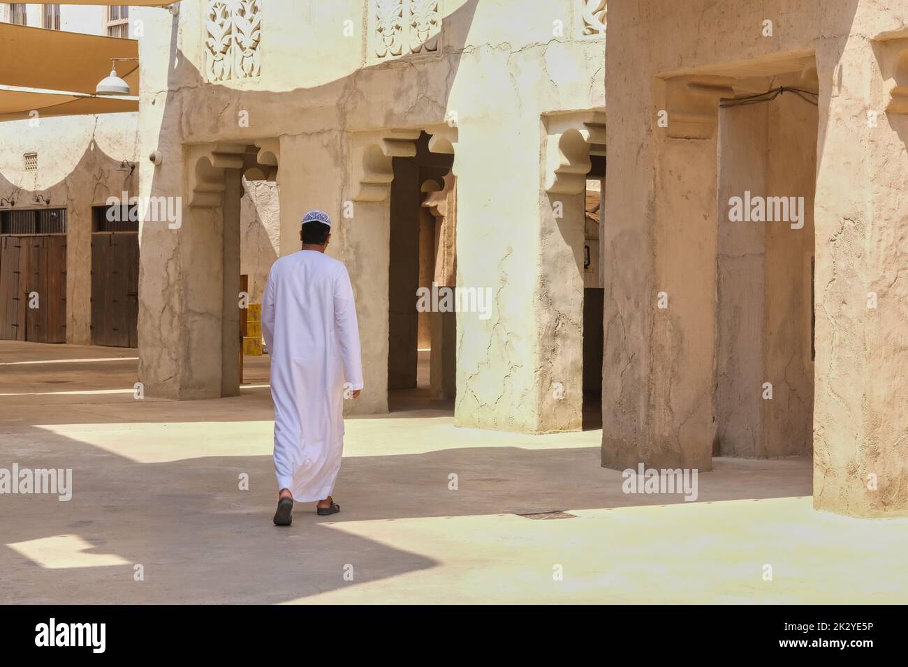 Vista posteriore su un uomo arabo non identificato che indossa abiti bianchi tradizionali mediorientali camminando nella città vecchia. Foto Stock