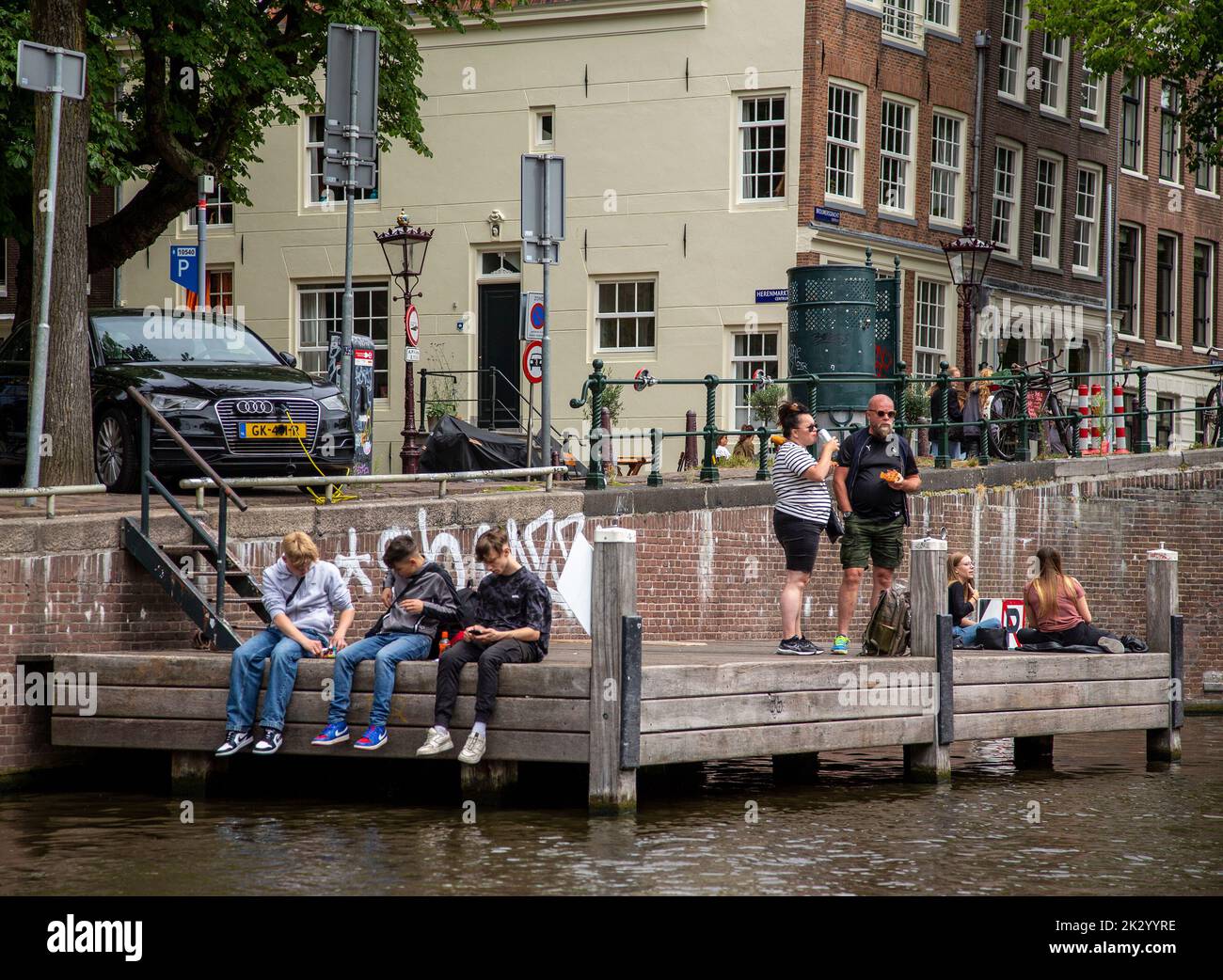 Ragazzi seduti su un molo accanto ad un canale di Amsterdam Foto Stock