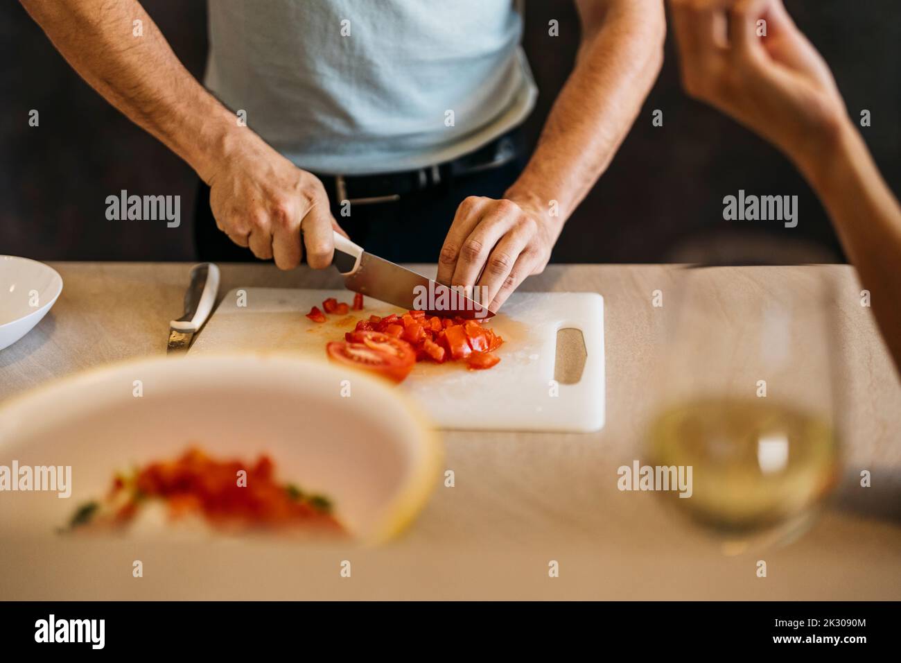 L'uomo caucasico taglia il pomodoro per un'insalata su un tritare in cucina Foto Stock