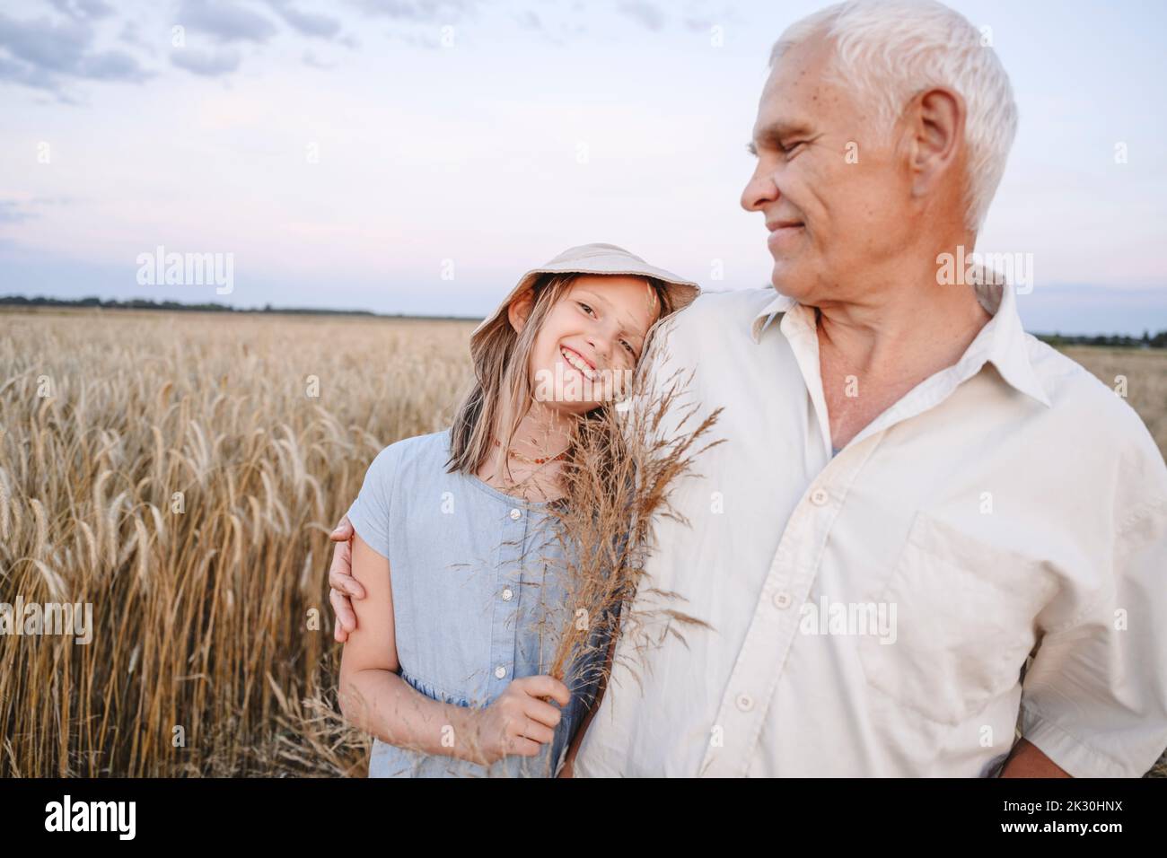 Ragazza sorridente che tiene raccolti con nonno in piedi al campo di segale Foto Stock