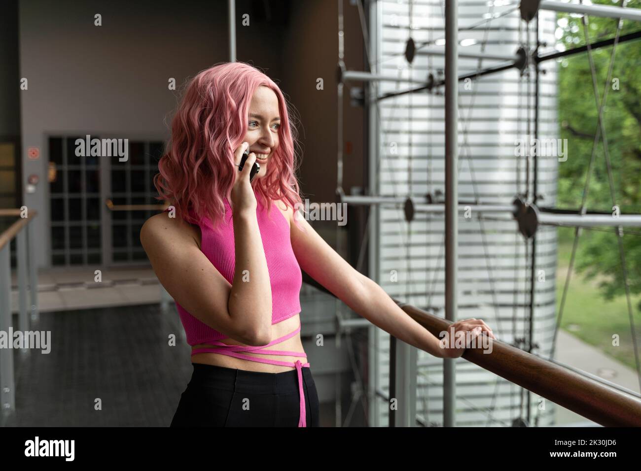 Donna felice con i capelli tinti rosa che parlano sul telefono cellulare da ringhiera Foto Stock