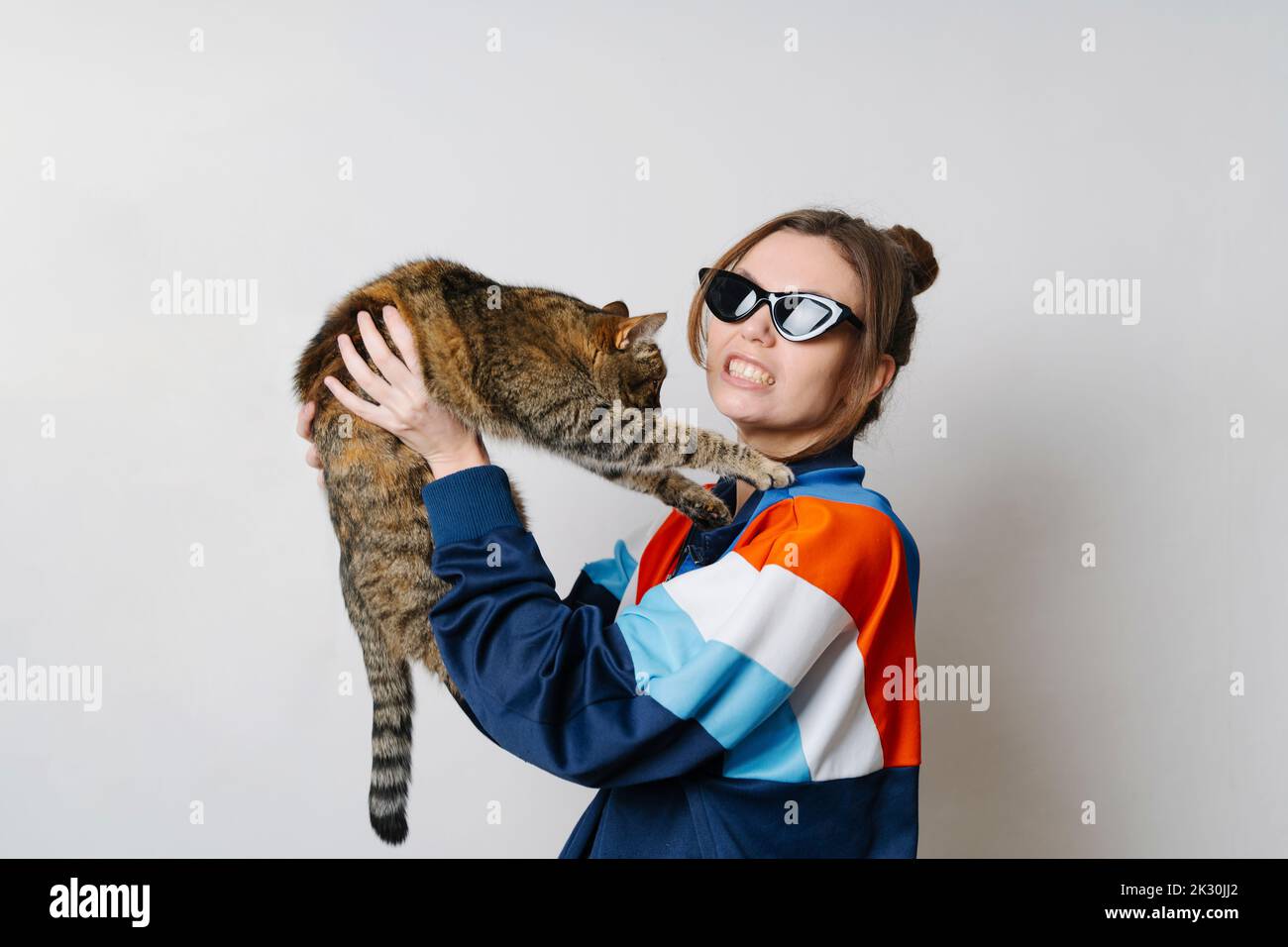 Giovane donna con gatto che stringe i denti su sfondo bianco Foto Stock