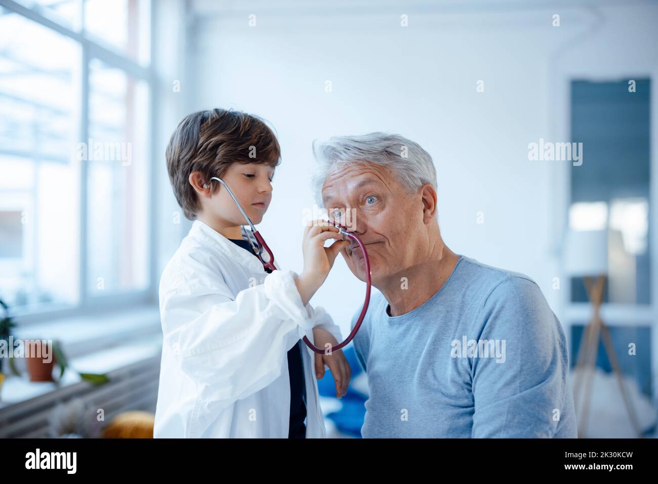 Ragazzo imitato come medico che controlla il naso del nonno con stetoscopio a casa Foto Stock