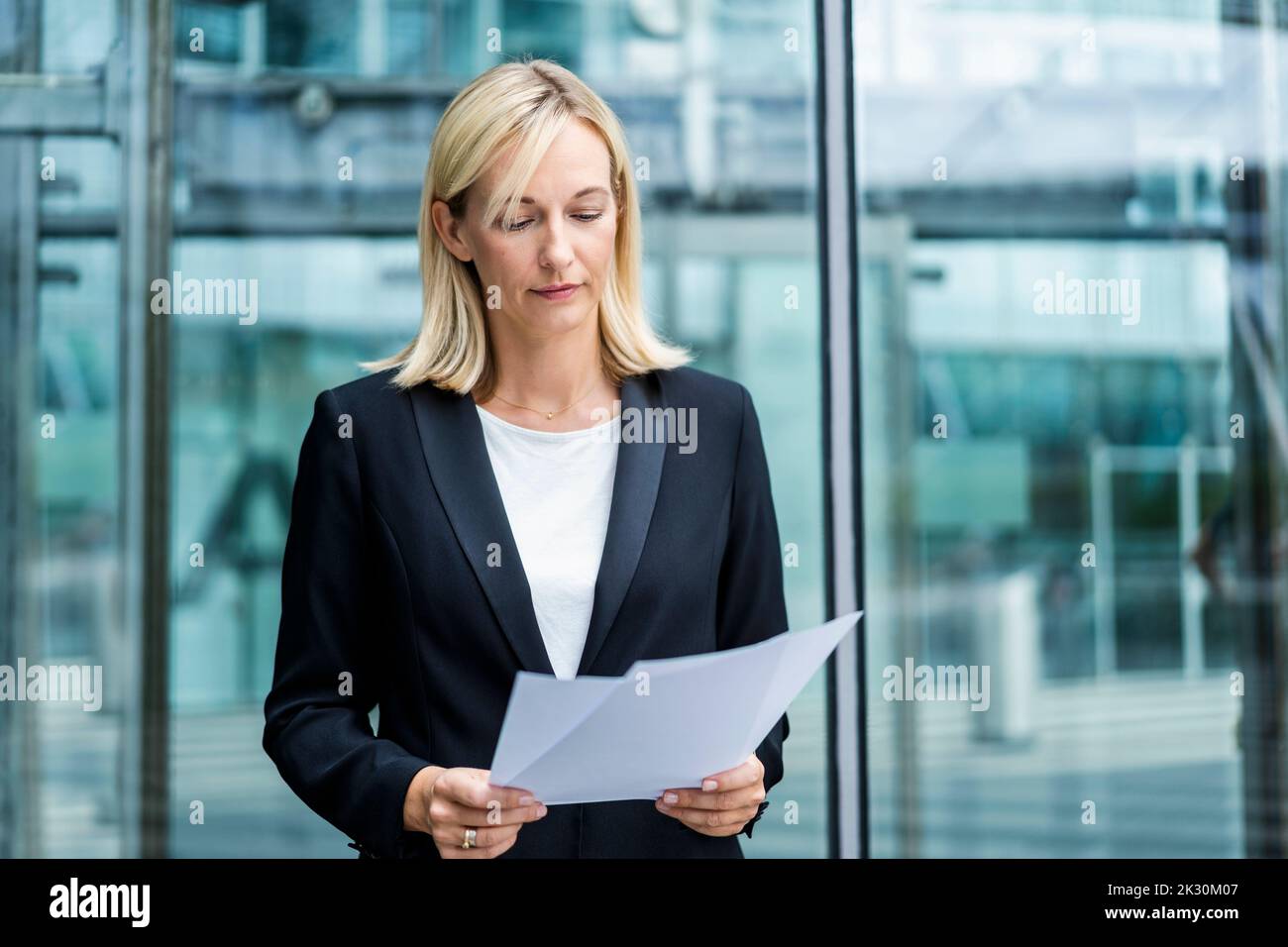 Una donna d'affari che legge i rapporti d'affari in piedi davanti all'edificio Foto Stock