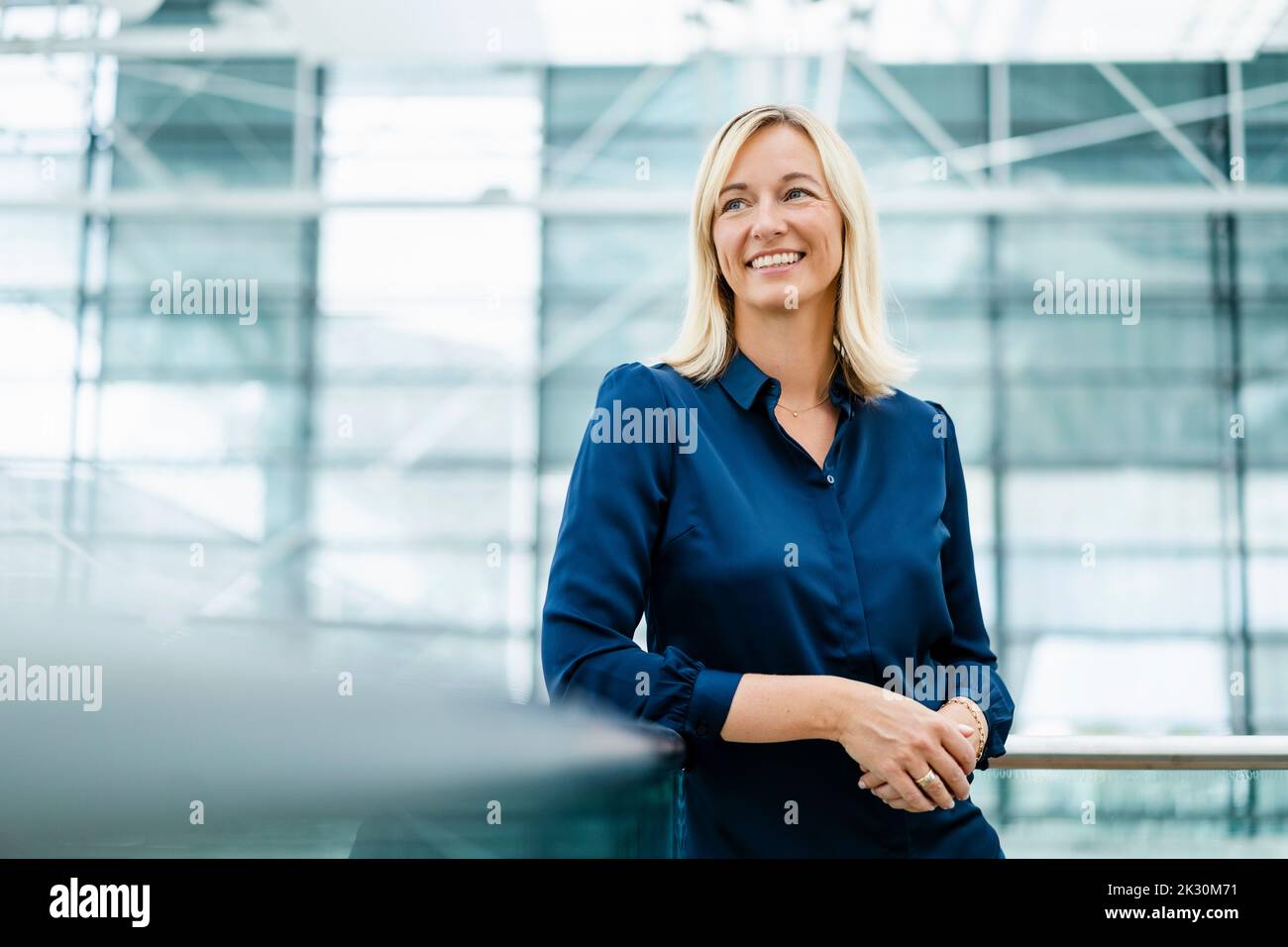 Donna d'affari sorridente con capelli biondi appoggiati alla ringhiera Foto Stock