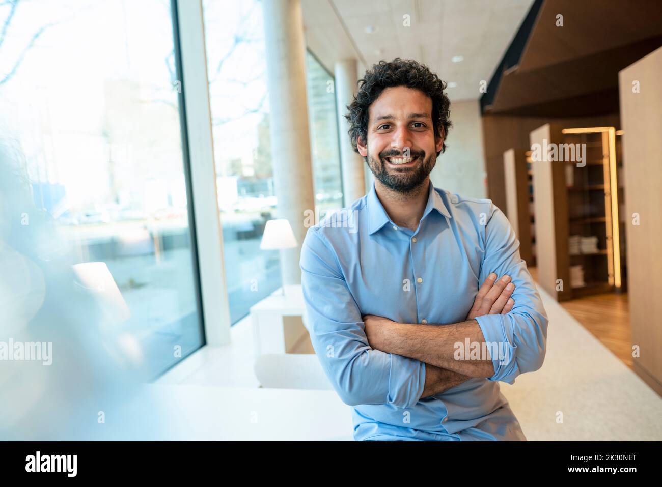 Uomo felice con le armi incrociate in biblioteca Foto Stock