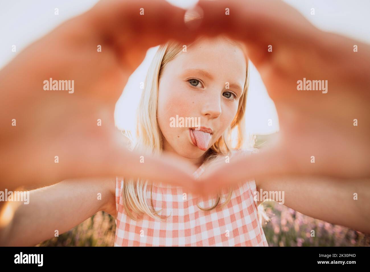 Ragazza che si stacca la lingua facendo gesto a forma di cuore Foto Stock