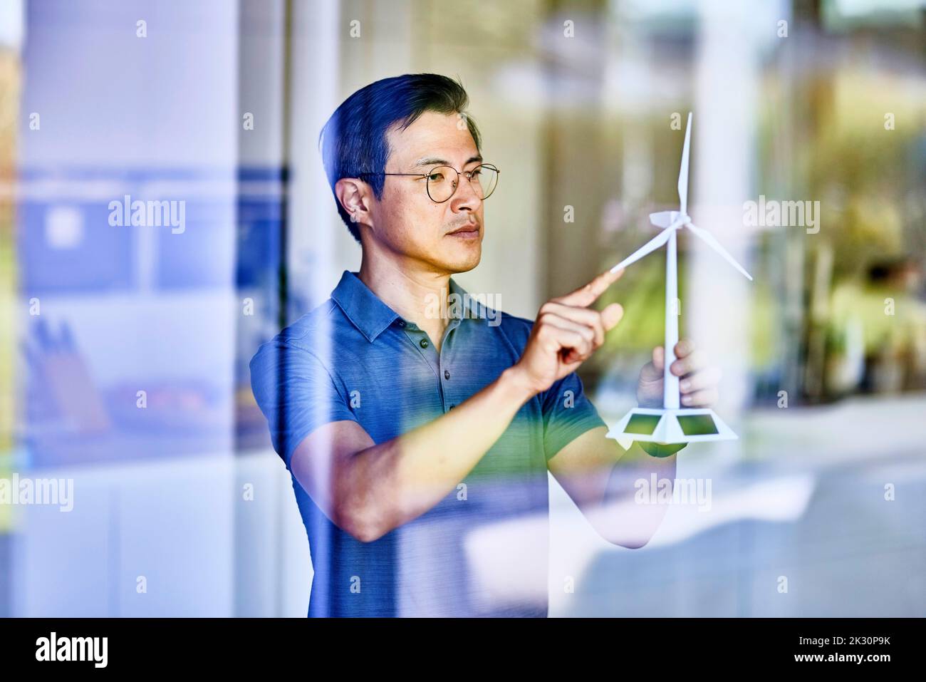 Uomo che esamina il modello di turbina eolica visto attraverso il vetro Foto Stock