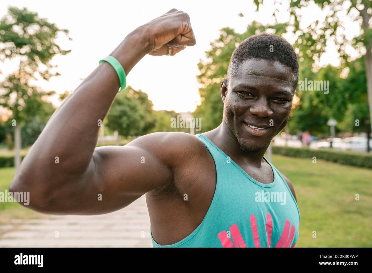 Giovane uomo sorridente che flette i muscoli al parco Foto Stock