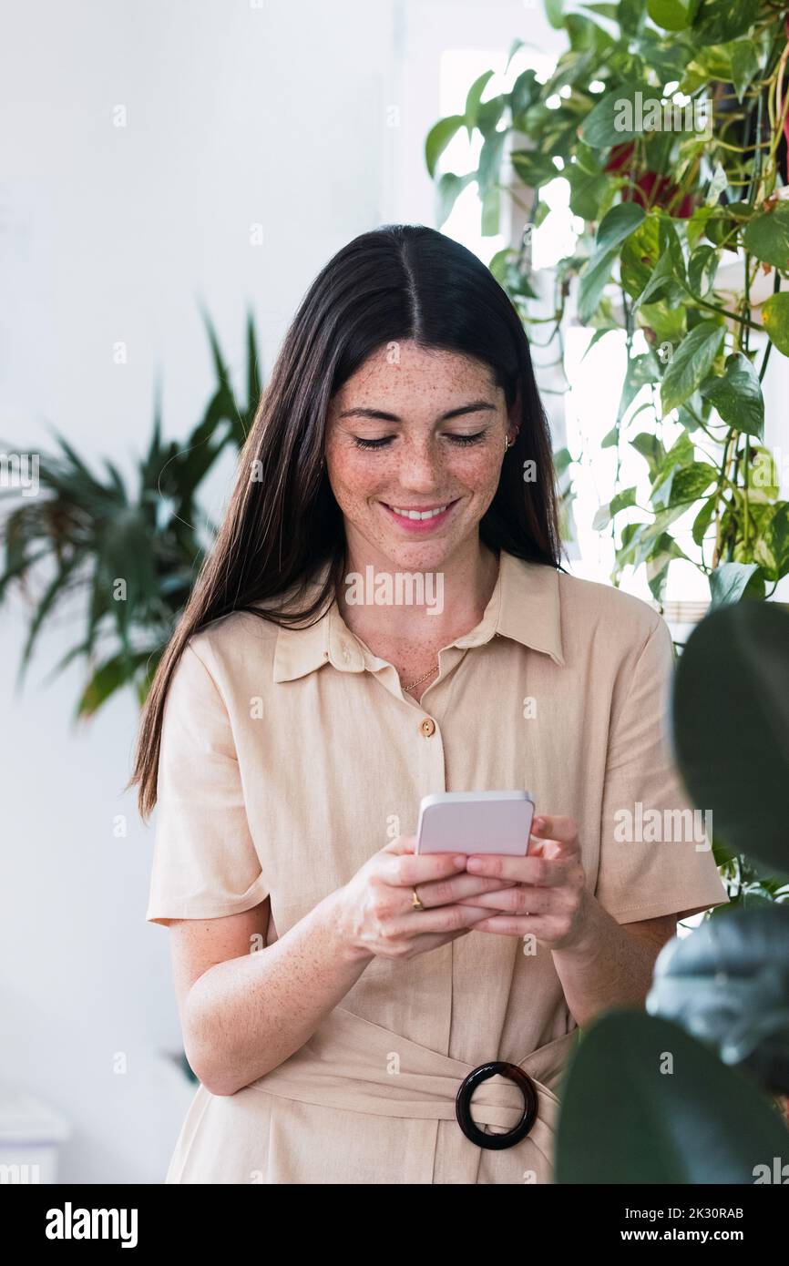 Sorridente giovane imprenditrice della messaggistica di testo attraverso smart phone in office Foto Stock