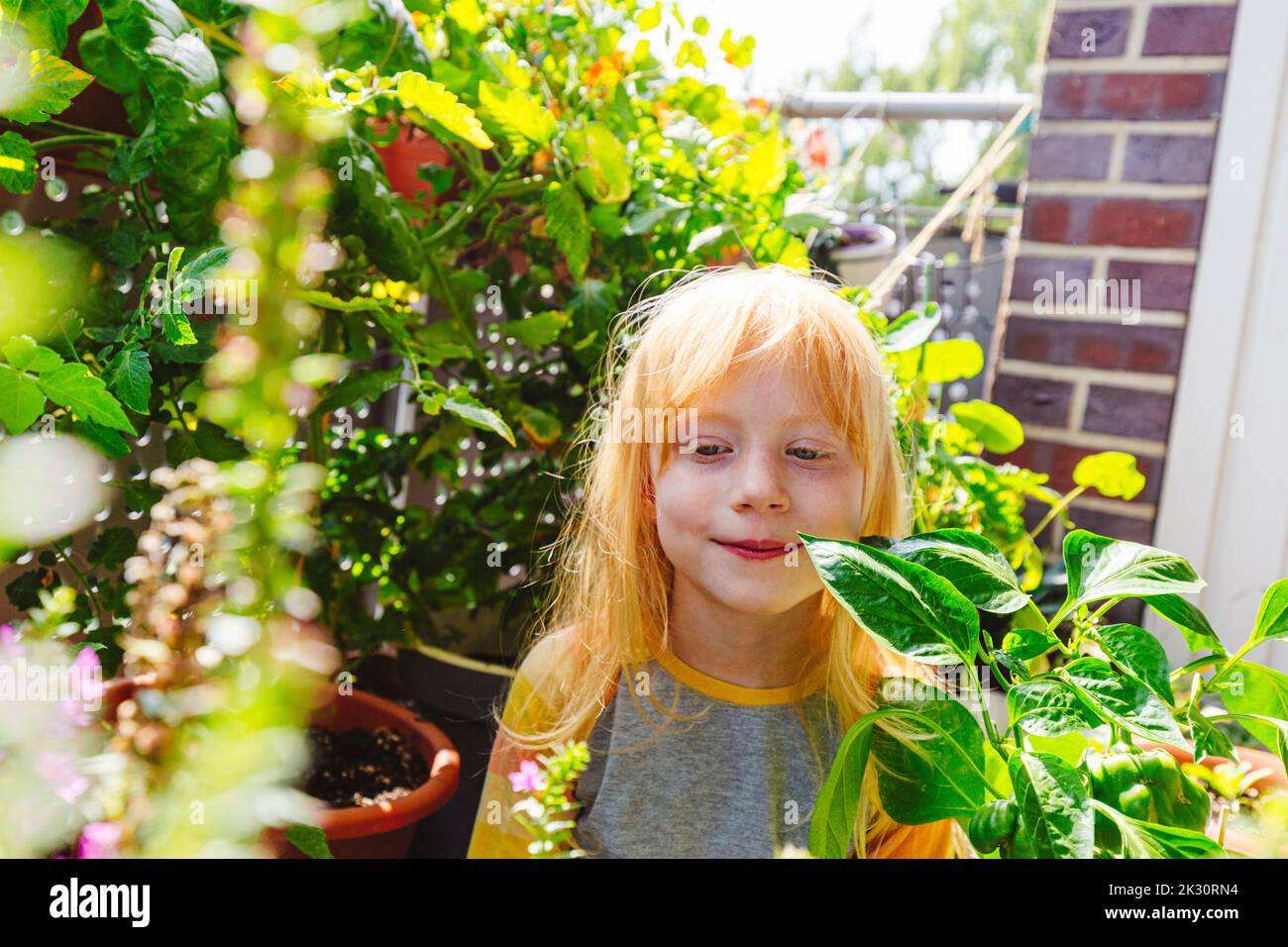 Ragazza sorridente in piedi in mezzo alla pianta nel balcone Foto Stock