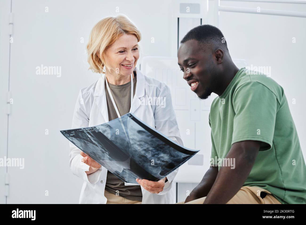 Medico sorridente che tiene radiografie guardando il paziente in clinica Foto Stock