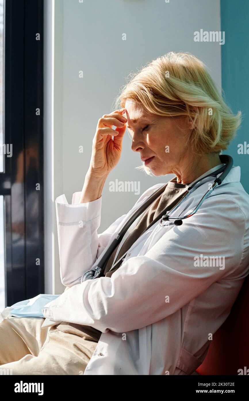 Medico esausto con capelli biondi seduti in clinica Foto Stock