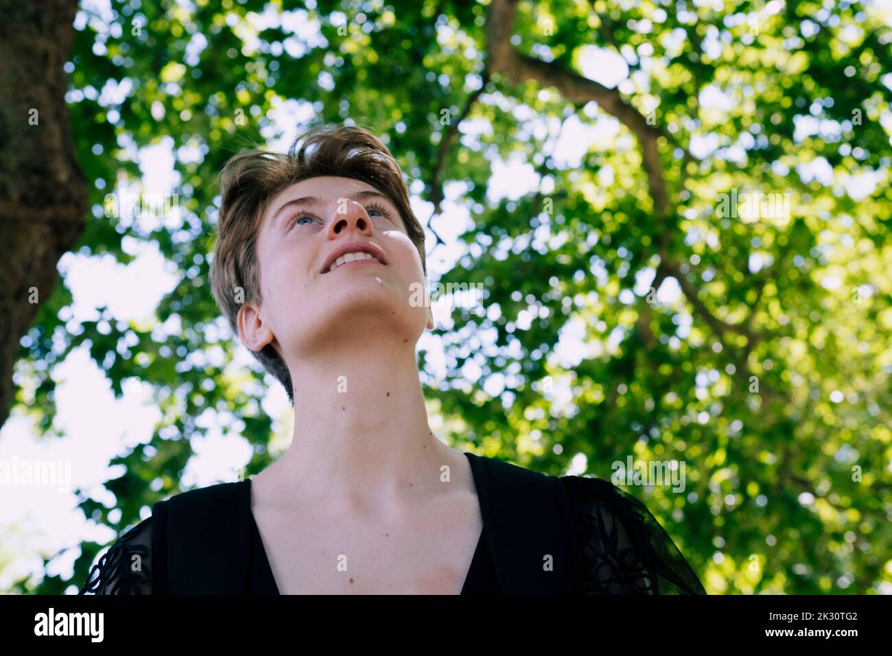 Felice non-binaria persona in piedi sotto l'albero Foto Stock