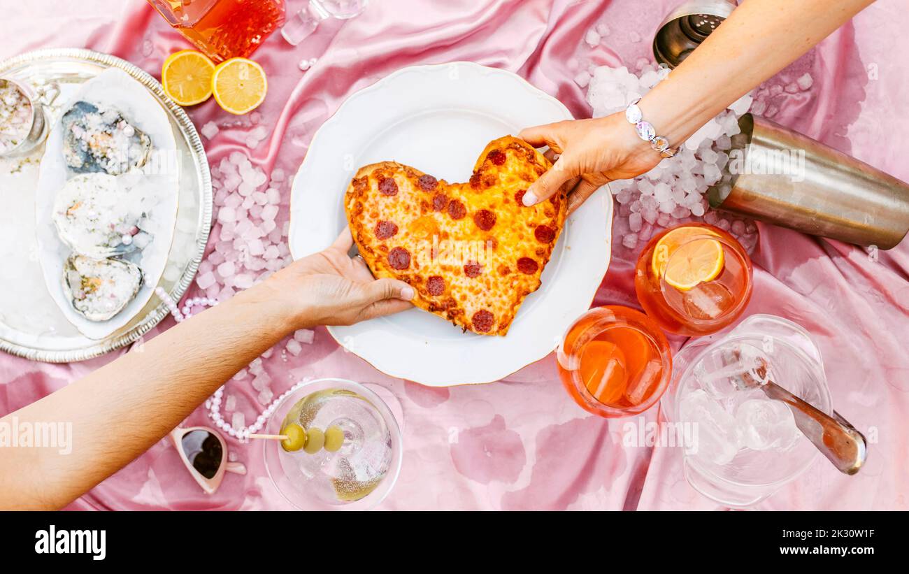 Mano delle donne che tirano la pizza a forma di cuore a tavola Foto Stock