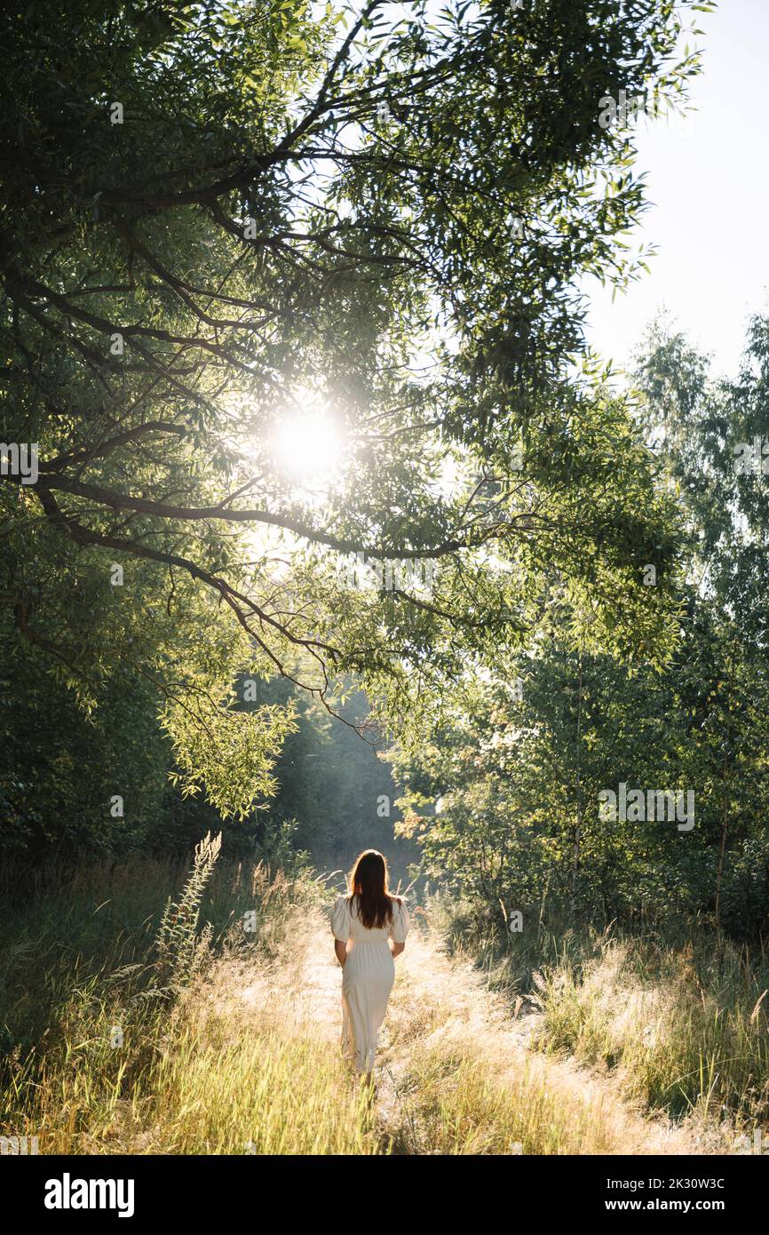 Donna che indossa un abito bianco a piedi nella foresta Foto Stock