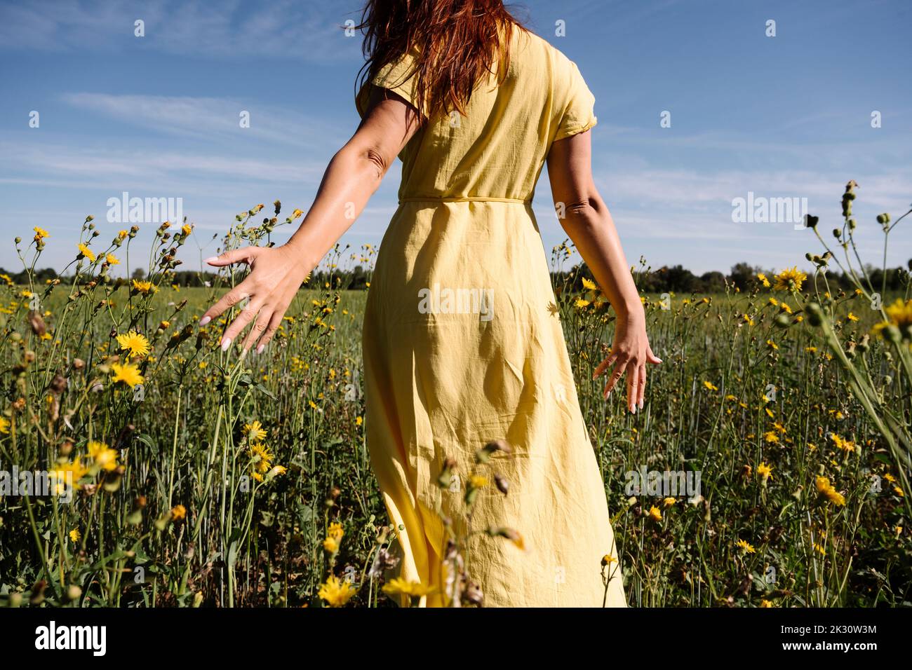 Donna in abito giallo che cammina tra i fiori Foto Stock