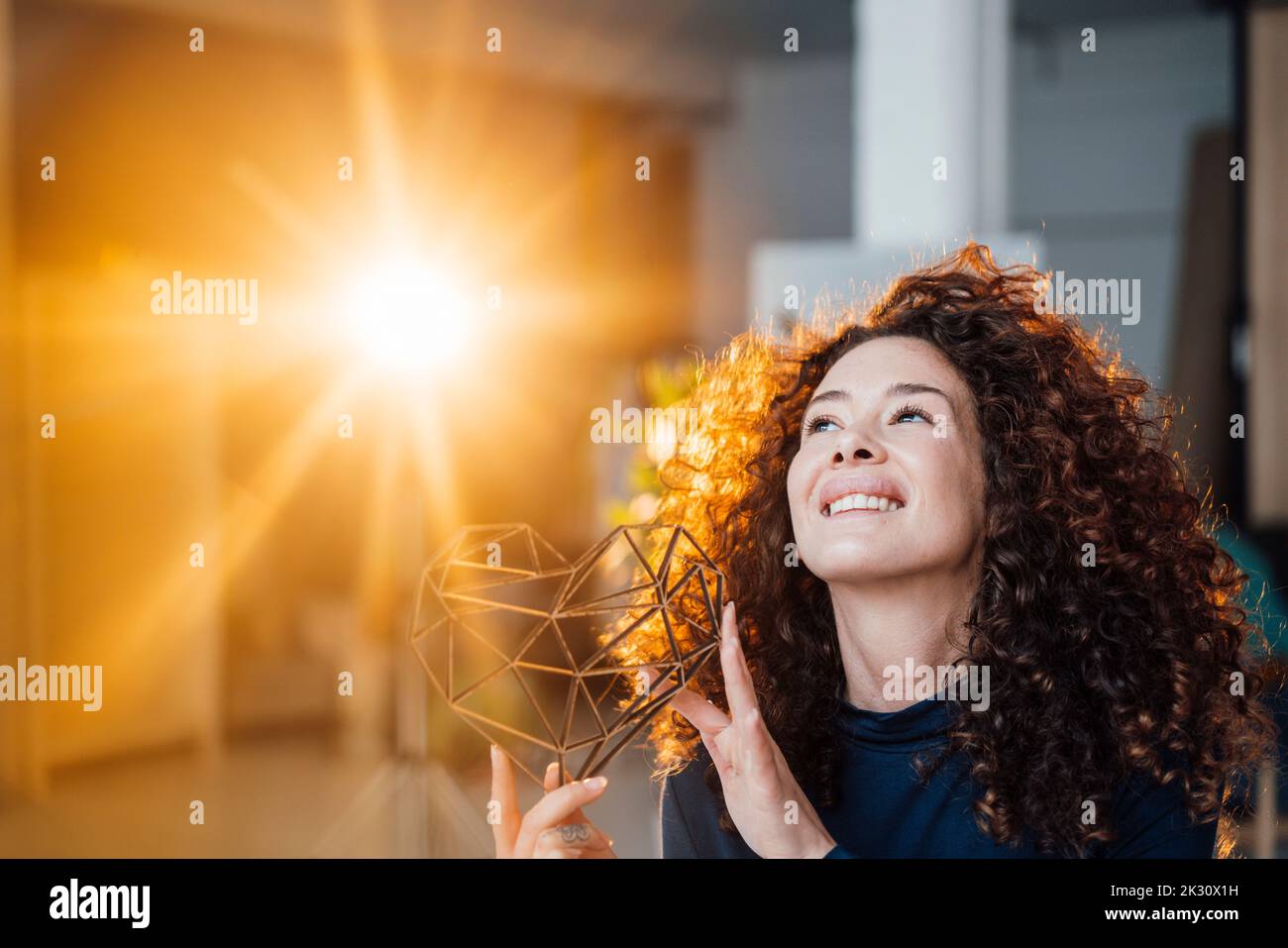 Donna sorridente con capelli ricci tenendo modello a forma di cuore Foto Stock