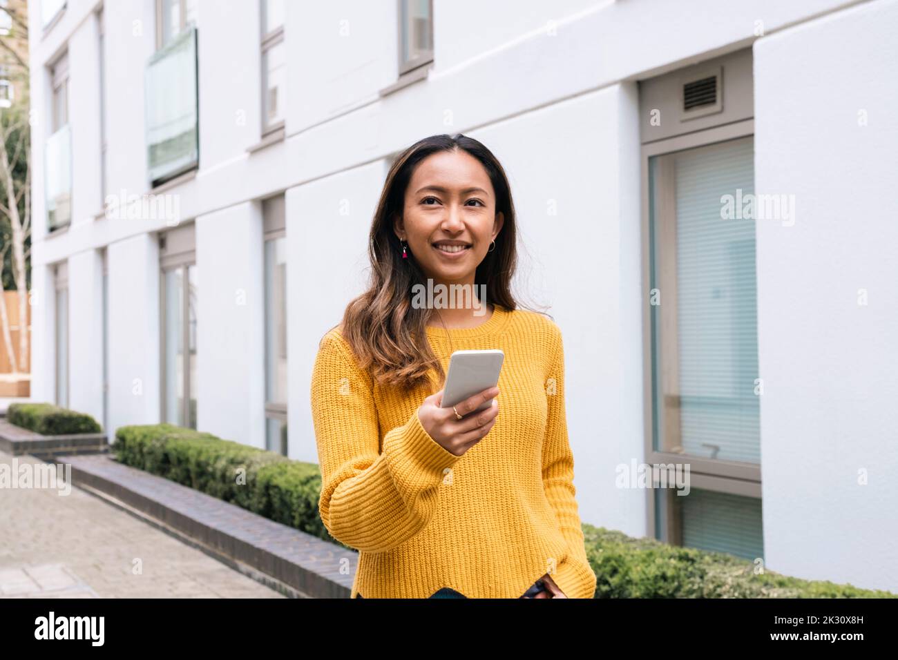 Felice giovane donna che tiene il telefono cellulare da costruzione Foto Stock